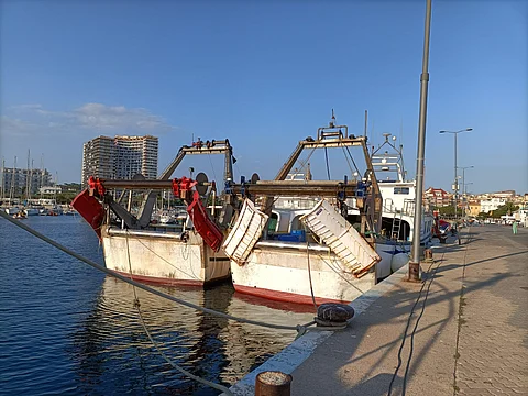 Two trawler vessels with flying doors docked in a Mediterranean port in Spain.