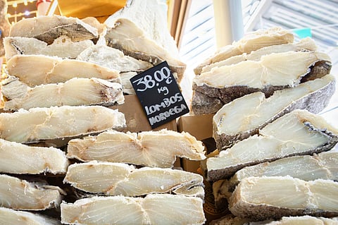 A large stack of premium, thick-cut, salted and dried codfish (Bacalhau) fillets on display with a handwritten price tag at the Mercado do Bolhão in Porto.