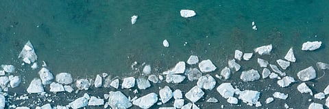 Top view of the white ice floes on the shore and in the blue sea water. Aerial view of melting ice on the sea coast. Climate change in the Arctic. Northern nature. Beautiful wide panoramic background.
