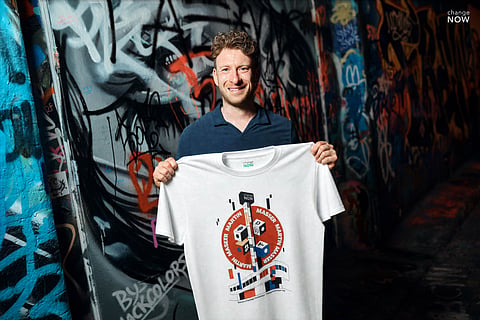 Martin Masser, ChangeNOW’s Director of Strategic Partnerships, holds a branded T-shirt in a graffiti-covered London passage.