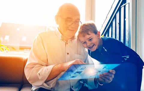 Concept of internet of things, where a digital smart screen controls household items like door locks, washing machine and surveillance camera. The screen looks futuristic and has a see through display. Senior man interacts with the touchscreen. Grandfather and grandson plays with the tablet and enjoy themselves.