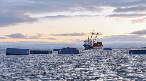 Containers floating on the water with the cargo ship Sivumut off in the distance