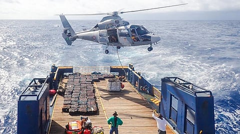 A French Navy helicopter hovers near the stern of the seized vessel. Note the bales containing the confiscated cocaine placed on the deck.