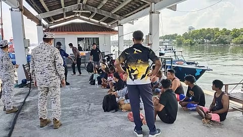 Malaysian Maritime Enforcement Agency personnel stand guard over 23 Indonesian nationals who had attempted to enter Malaysia illegally, May 11, 2026. Earlier on that same date, the boat carrying the detained Indonesians sank off Perak State. Sixteen other people who were on the boat have not yet been found.