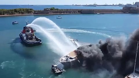 A tug attempts to extinguish the fire on the burning superyacht John in a marina in Brindisi, Italy, October 3, 2026.