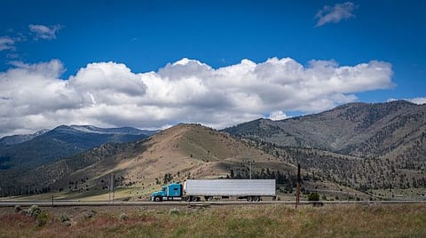 Photo of truck on scenic highway with mountains and cloudy skies, US
