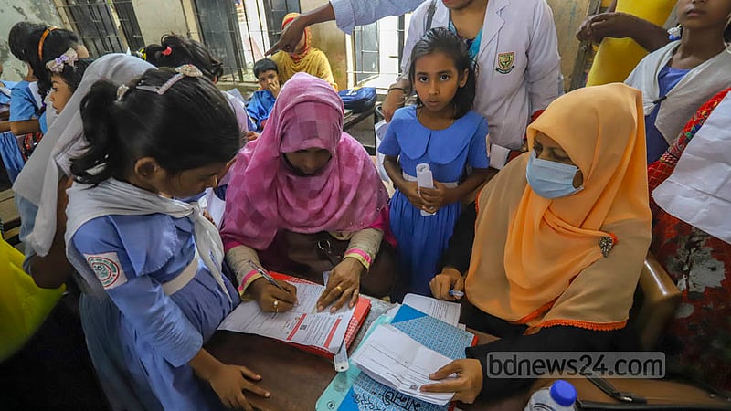Health officials check the COVID-19 vaccine cards of children before administering the shots at the Hazi Yousuf Ali Govt Primary School centre in Dhaka’s Kazipara.