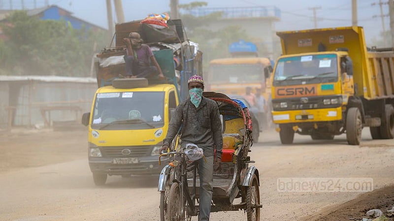 A rickshaw-puller covers his face with a piece of cloth and head with a prayer cap to save himself from dust on the Dhaka-Narayanganj Highway. A man sitting on a pick-up van behind the rickshaw also covers his face and head.
