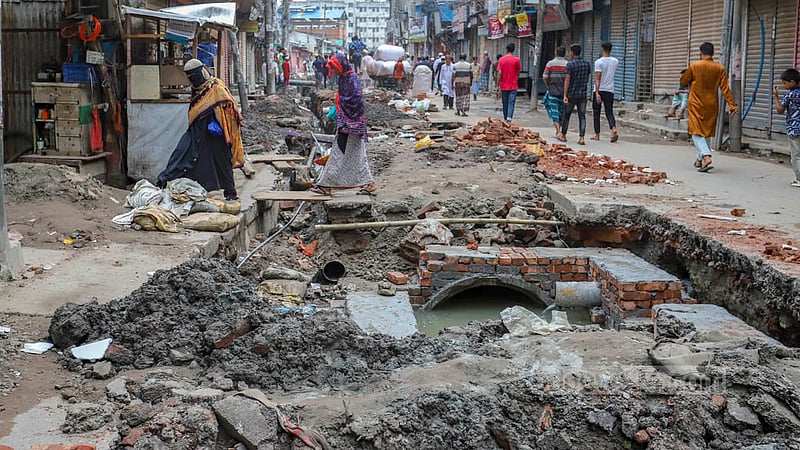 People walk from one side of the road to the other using wooden planks as the road in Old Dhaka’s Naya Bazar has been dug up for the installation of sewage and water pipes.