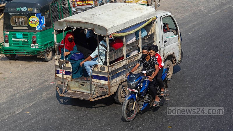 Two men, without wearing helmets, ride a motorcycle down the wrong side of the Dhaka-Chattogram Highway.