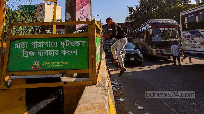 A jaywalker crosses the road by climbing over the road dividers with iron grids on Sunday, Oct 23, 2022, in Dhaka’s Mohakhali.