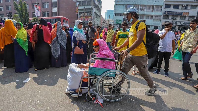 Relatives push an ill and elderly woman in a wheelchair as they pass through the site of garment factory workers’ protests demanding back pay in Dhaka’s Arambagh on Tuesday, Nov 1, 2022.Photo: Asif Mahmud Ove