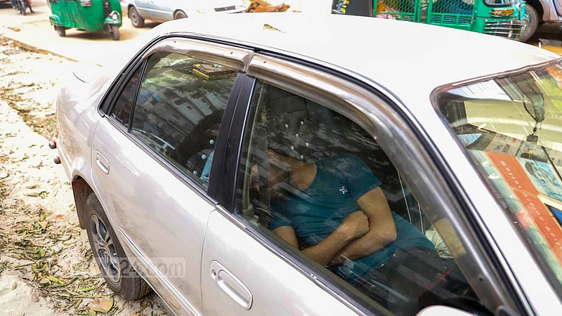 A man takes a nap inside a car parked on an unpaved section of the road connecting Gulshan and Mohakhali in Dhaka.
