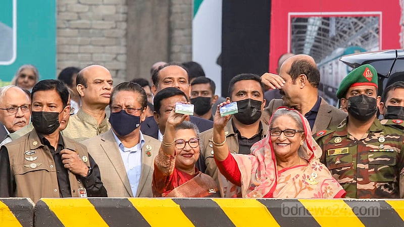 Prime Minister Sheikh Hasina and her sister Sheikh Rehana show their Mass Rapid Transit pass as they wave to the people who gathered at Agargaon to watch Bangladesh’s first metro train reach its destination from Uttara on the inaugural trip with the daughters of Bangabandhu on board on Wednesday, Dec 28, 2022. Photo: Asif Mahmud Ove