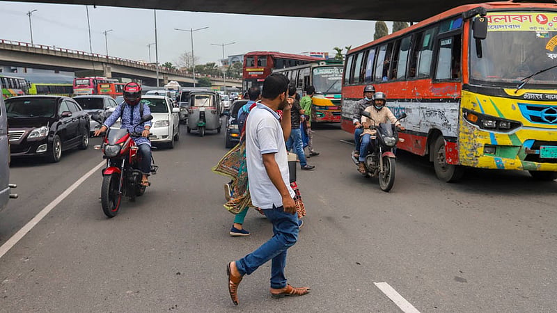 Candidates risk their lives to cross the busy Airport Road by scaling a traffic median and defying speedy vehicles in the MES area after bank recruitment exams on Friday, Mar 31, 2023. Photo: Tawhiduzzaman Tapu