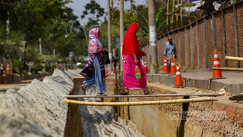 Women use an iron sheet to cross a hole as parts of Hatirjheel Link Road in Dhaka are being dug up for the installation of DPDC cables.