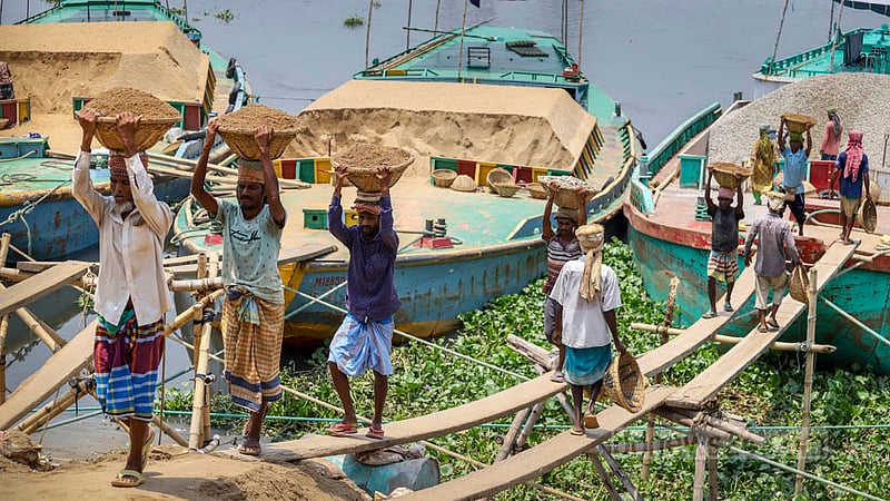 Labourers unload coal, rocks and sand from a cargo vessel in the Gabtoli docks of Dhaka on Sunday, Apr 30, 2023, the eve of International Workers’ Day or May Day. Photo: Asif Mahmud Ove