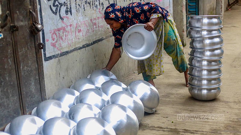 A woman leaves aluminium utensils made in a factory out in the sun to dry in Dhaka’s Kamrangirchar on Friday, May 26, 2023. Photo: Tawhiduzzaman Tapu