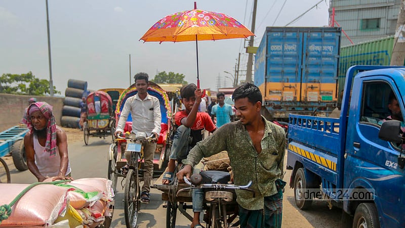 A child holds an umbrella over a three-wheeler driver's head amidst the scorching afternoon heat on Tuesday, Jun 6, 2023. Photo: Tawhiduzzaman Tapu