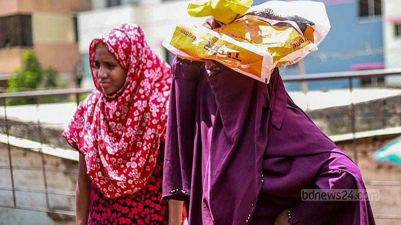 A woman holds a shopping bag over her head to get some respite from the blazing sun in Dhaka’s Mohammadpur on Sunday, Jul 23, 2023. Photo: Tawhiduzzaman Tapu