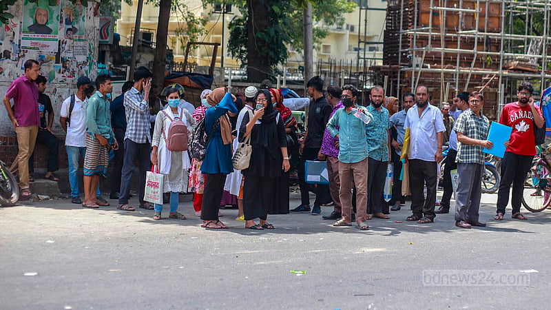 Commuters take shelter from the sun under a tree while waiting for buses at Dhaka’s Shahbagh intersection on Thursday, Jul 20, 2023. Photo: Tawhiduzzaman Tapu
