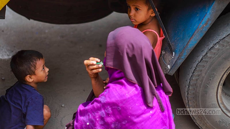 A woman allows her children to take shelter under an OMS truck to get some respite from the blazing sun in Dhaka’s Mohammadpur on Sunday, Jul 23, 2023. Photo: Tawhiduzzaman Tapu