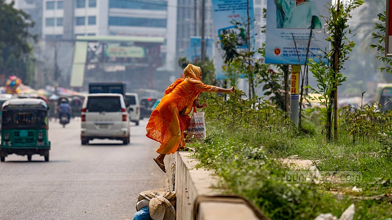 A woman carrying a child awkwardly climbs over the road divider in front of NITOR, risking her life as well as that of the child in the process. Photo: Mahmud Zaman Ovi
