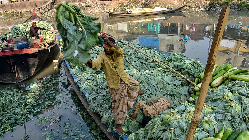 Two workers offload cabbages, a winter vegetable, from a boat at the Chaktai Wholesale Market in Chattogram.