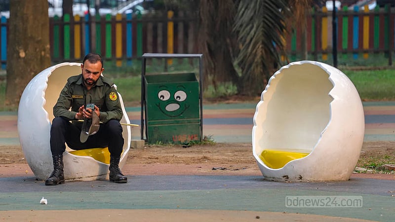 In Dhaka's Ramna Park, an Ansar member occupies an egg-shaped chair in the Children's Corner, engrossed in his mobile phone.