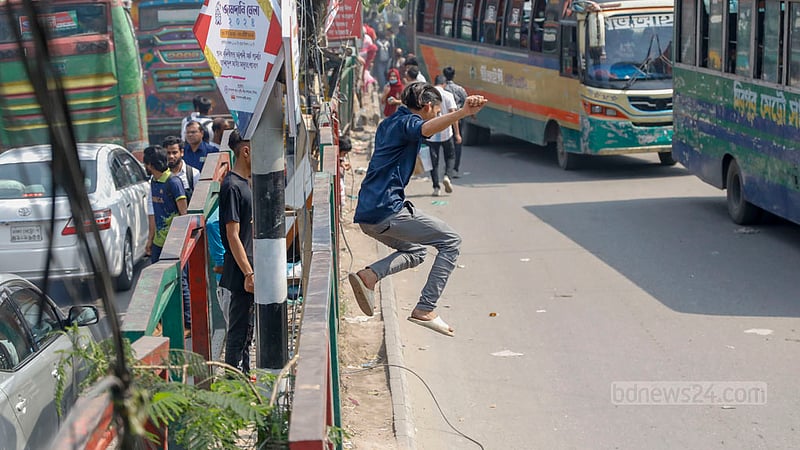 A youth jumps to cross the road through the road divider in Dhaka’s New Market area.