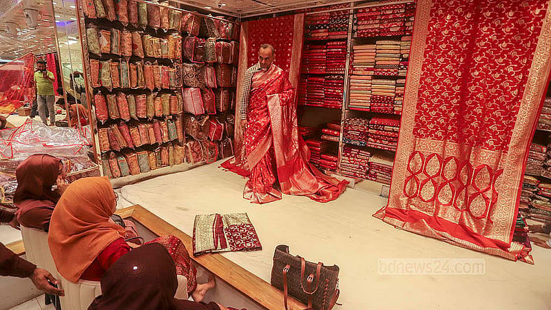 A trader shows of a saree for a potential customer at a store at Benarasi Palli in Dhaka’s Mirpur. Sales are heating up ahead of Eid-ul-Fitr. Photo: Abdullah al Momin