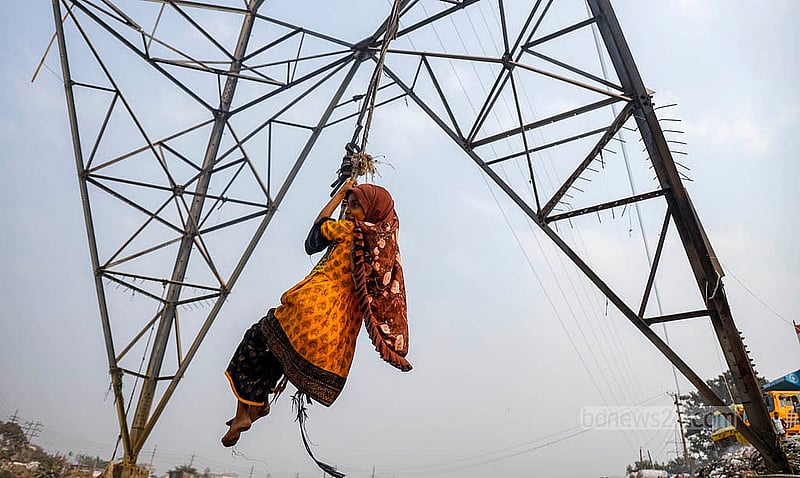 A child swings from a rope tied to an electricity pole beside the iron bridge in Dhaka’s Kamrangirchar, with garbage floating in the Buriganga River below. Photo:  Mahmud Zaman Ovi