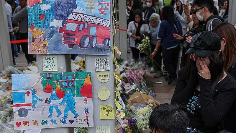 A woman wipes her eyes at a makeshift memorial at Wang Fuk Court housing complex to pay tribute to victims, following a deadly fire, in Tai Po, Hong Kong, China, Nov 30, 2025. REUTERS/Tyrone Siu