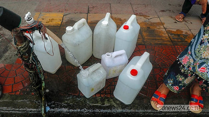 Locals collect water in plastic bottles, drums, and gallon jars at a tap on the footpath in front of the Bangabhaban Colony’s No. 5 gate on Dhaka’s Ittefaq Intersection. Photo: Abdullah Al Momin