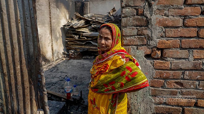 Burnt tin sheets are heaped inside the remains of a home, while a woman waits outside hoping for assistance. Photo: Mahmud Zaman Ovi