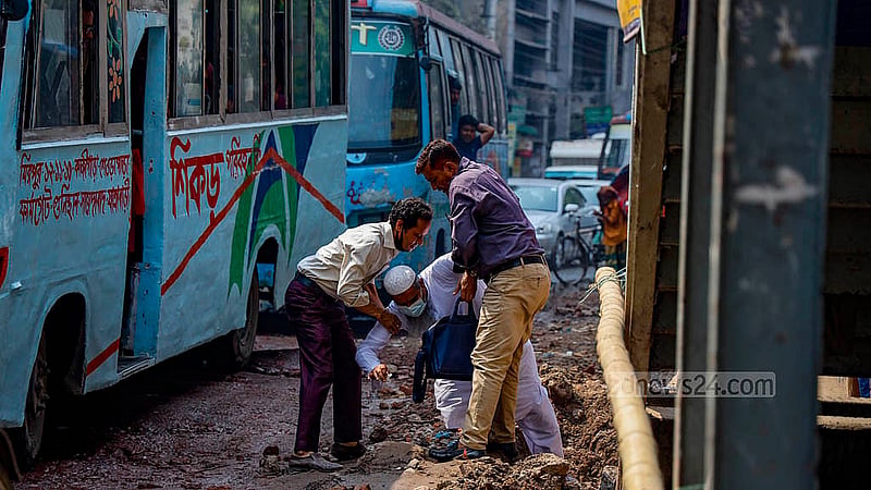 Footpaths have been dug next to the road near the Tikatuli footbridge in Dhaka. Two pedestrians are helping a man who tripped while walking to stand back up. Photo: Mahmud Zaman Ovi