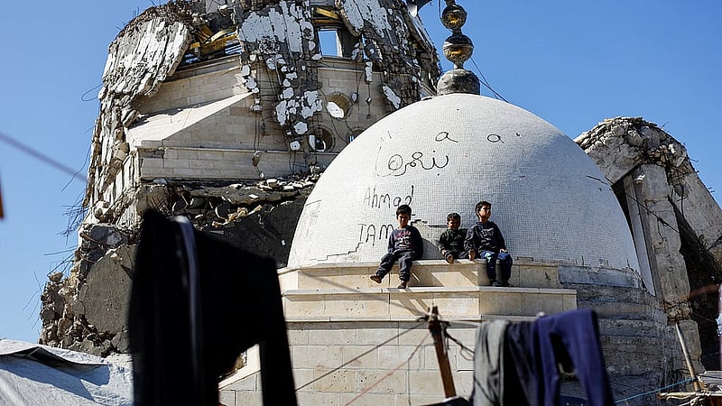 Palestinian children sit atop the rubble of a mosque destroyed during the two-year Israeli offensives, which is surrounded by tents for displaced Palestinians, in Gaza City, Feb 11, 2026. REUTERS/Mahmoud Issa