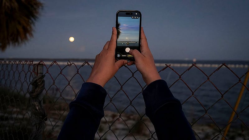 A woman uses her phone to take photos of the moon after the launch of the next-generation moon rocket, the Space Launch System (SLS) rocket and the Orion crew capsule, part of NASA's Artemis II lunar flyby mission, from NASA's Kennedy Space Center, in Titusville, Florida, U.S., April 1, 2026. Photo: Reuters