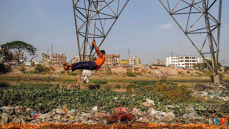 A child swings from a rope tied to an electric pole near the iron bridge in Kamrangirchar, as heaps of garbage float in the polluted waters of the Buriganga River below.Photo: Mahmud Zaman Ovi