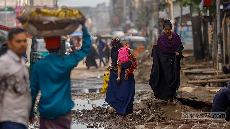 A woman carrying a child walks along the uneven, broken road. The road from Postogola Bridge to Jatrabari intersection has been in such poor condition for a long time. Photo: Mahmud Zaman Ovi