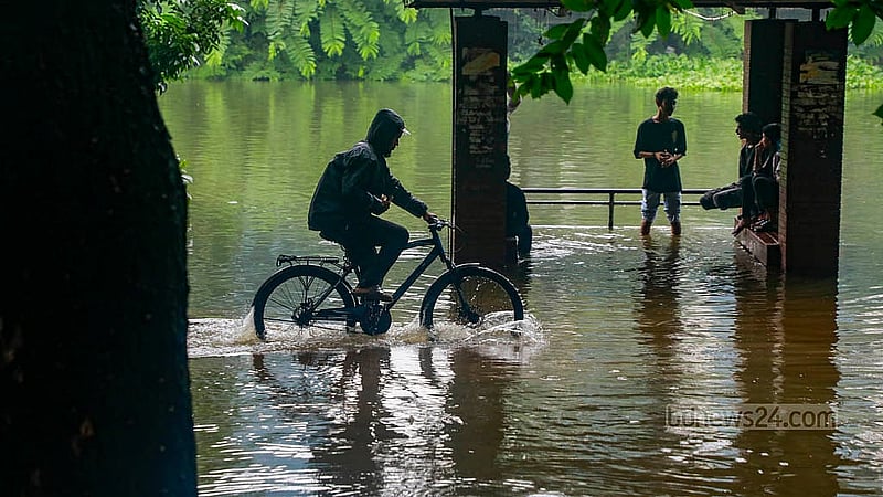 Dhaka’s Dhanmondi Lake is submerged in rainwater. A man rides his bicycle through the overflowing water along the walkway. Photo: Mahmud Zaman Ovi