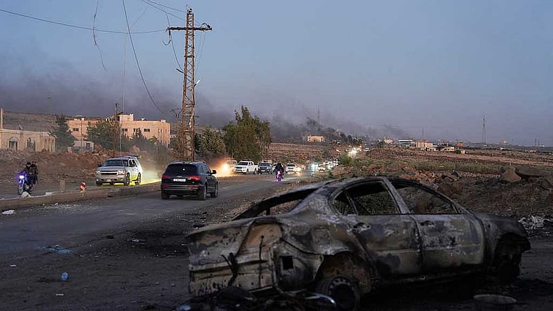Smoke rises as a damaged car remains along a street, as Sweida province has been engulfed by nearly a week of violence triggered by clashes between Bedouin fighters and factions from the Druze, at Sweida governorate, Syria, July 18, 2025. REUTERS