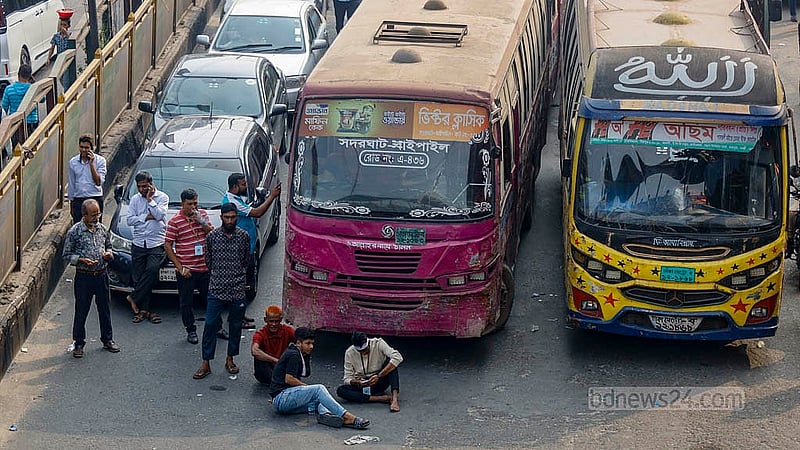 Mobile phone traders block the road outside Jamuna Future Park on Tuesday, Dec 2, 2025, sitting in front of vehicles to prevent traffic movement during their protest. Photo: Mahmud Zaman Ovi