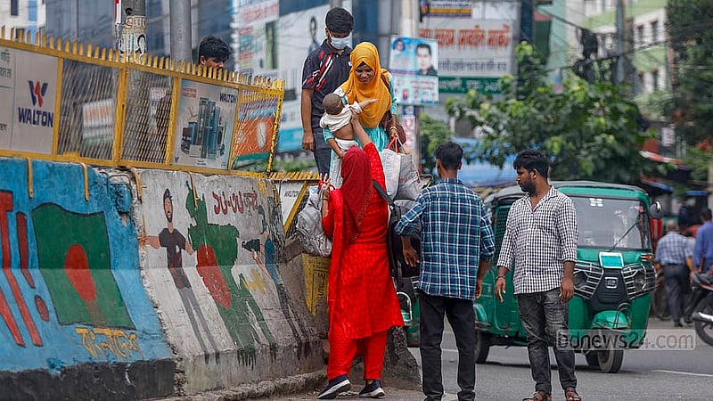 In Dhaka’s Mohakhali, two women, one carrying a small child, are scaling a tall road divider topped with iron fencing, ignoring safety measures meant to prevent such risky crossings. Photo: Mahmud Zaman Ovi