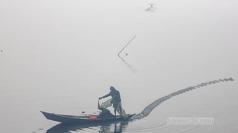A fisherman uses a small wooden dinghy to cast banned China duari in the Dhaleshwari River on a foggy morning. Photo: Mahmud Zaman Ovi