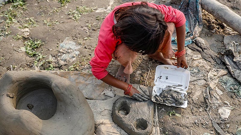 On the riverbank in Kamrangirchar, a mother shapes clay stoves to earn a living, while her child plays nearby with mud, mimicking the work.Photo: Mahmud Zaman Ovi