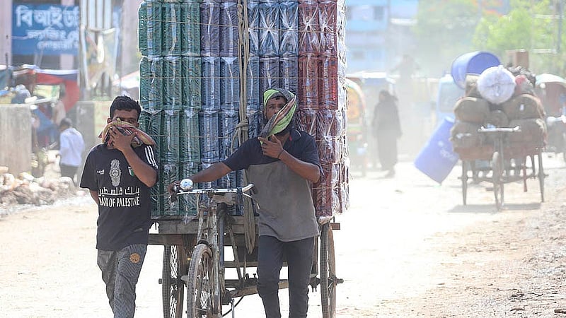Two men are seen covering their noses with a towel while transporting goods on a van, due to the extreme dust pollution on Beribadh Road. Photo: Abdullah al Momin