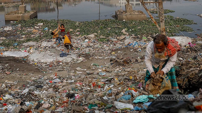 A group of children swing from a rope tied to an electricity pole beside the iron bridge in Kamrangirchar, while a man searches through plastic waste nearby. Photo:  Mahmud Zaman Ovi