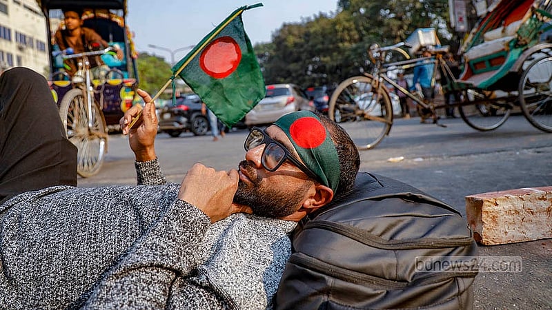 A member of Chhatra Shakti lies on the road with a flag while blocking the Shahbagh intersection on Monday, Dec 15, 2025, as part of protests demanding the resignation Home Advisor Jahangir Alam Chowdhury following the shooting of Sharif Osman bin Hadi. Photo: Mahmud Zaman Ovi