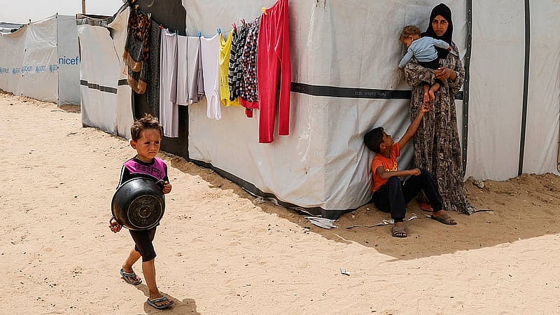 A child walks with a pot next to a woman holding a baby, as Palestinians wait to receive food cooked by a charity kitchen, in Khan Younis, southern Gaza Strip, April 6, 2025. Photo: Reuters